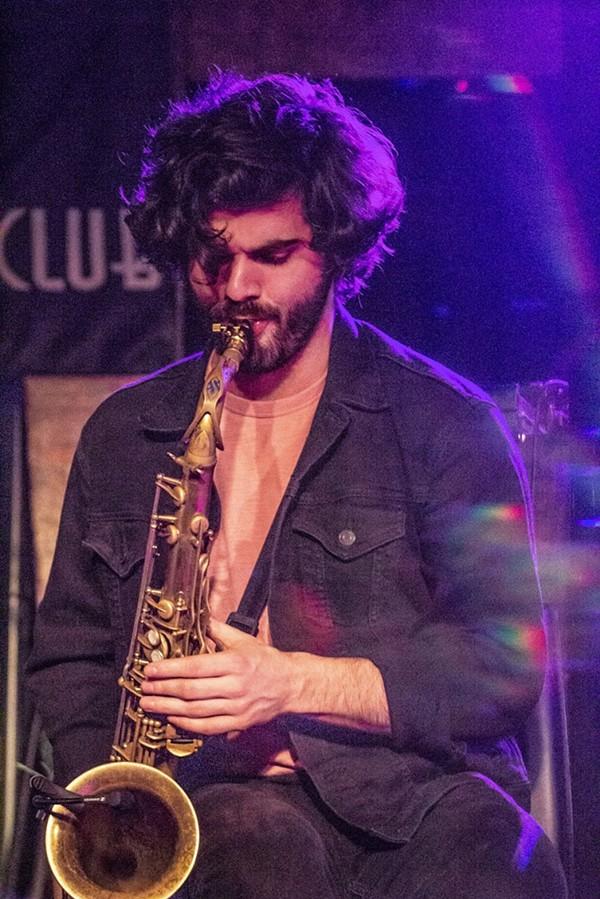 A man with curly hair plays a saxophone
