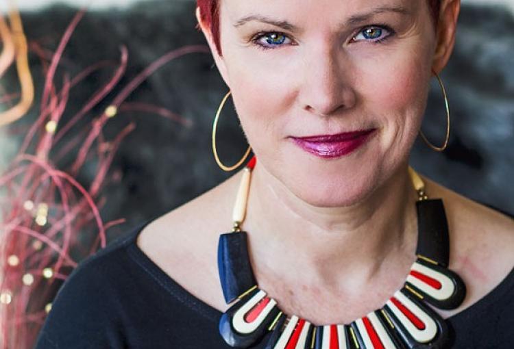 A woman with short red hair, hoop earrings, and a statement necklace