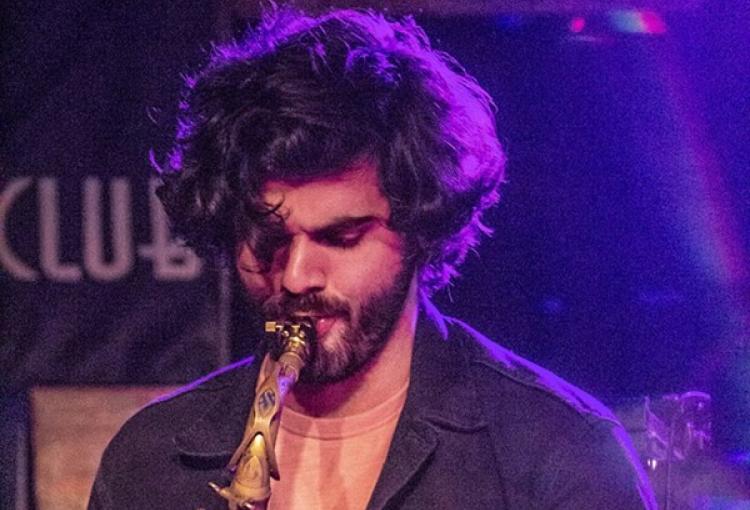 A man with curly hair plays a saxophone