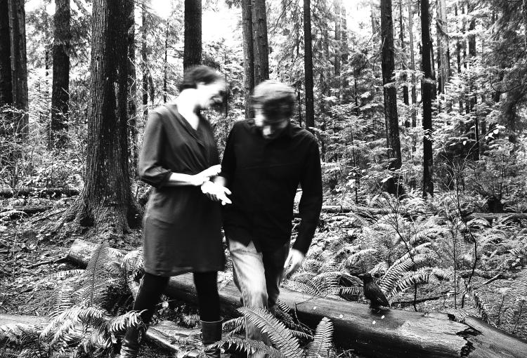 Black and white photo of two people walking through the woods